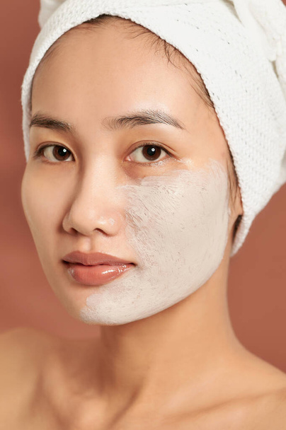 Spa menina asiática aplicando máscara de barro facial. Tratamentos de beleza. Sobre fundo azul
. - Foto, Imagem