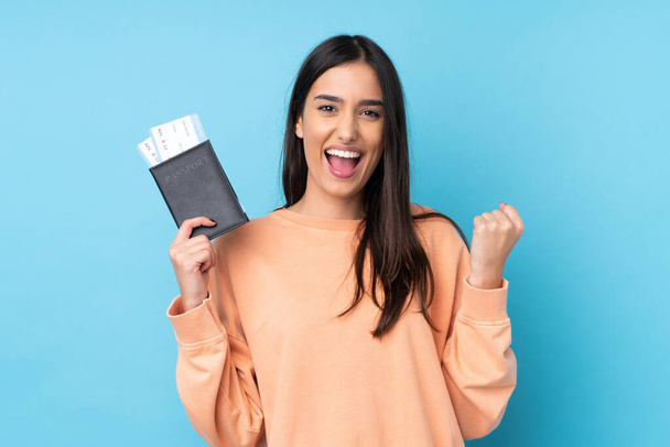 Young brunette woman over isolated blue background happy in vacation with passport and plane tickets - Φωτογραφία, εικόνα