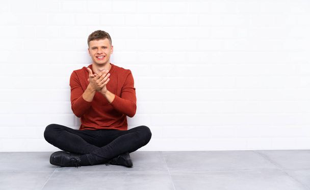 Fiatal jóképű férfi ül a padlón tapsolva - Fotó, kép