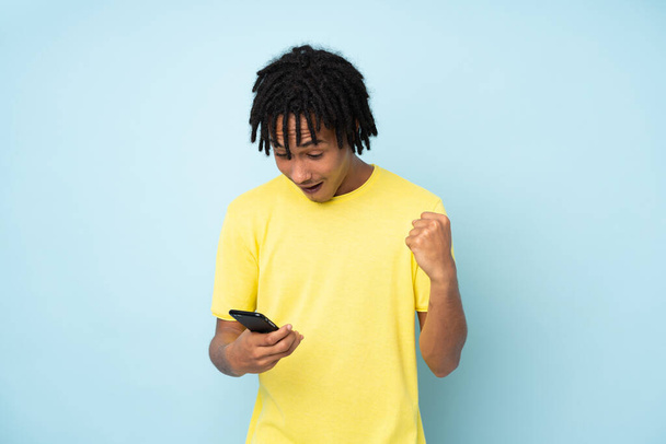 Young african american man isolated on blue background surprised and sending a message - Фото, зображення
