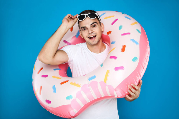 Young man with inflatable donut on blue background - Valokuva, kuva