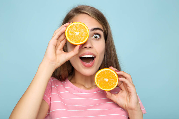 Young girl with fresh orange fruit on blue background - 写真・画像