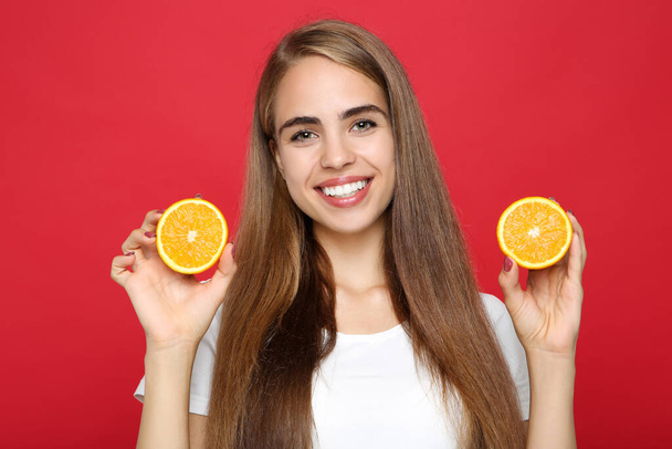 Young girl holding fresh orange fruit on red background - Foto, afbeelding