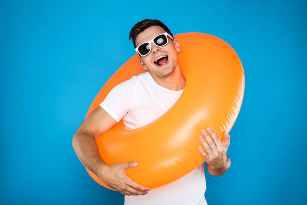 Young man with inflatable ring on blue background - Fotó, kép