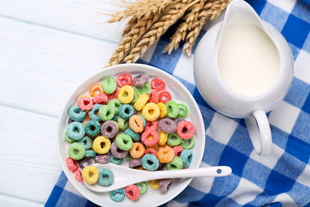 Colorful corn rings in bowl with milk and wheat ears on wooden table - Фото, зображення