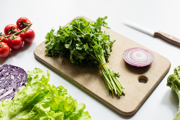 surtido de verduras frescas y tabla de cortar de madera con cebolla roja y perejil sobre fondo blanco - Foto, imagen