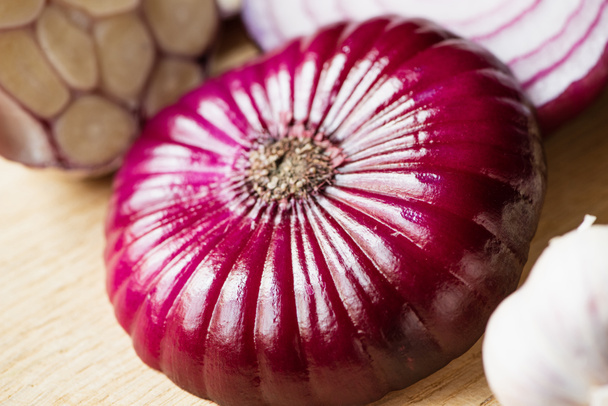 close up view of red onion and garlic on wooden cutting board - Foto, Bild