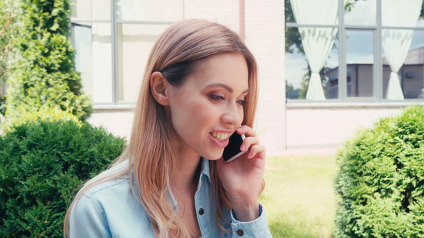 Cheerful student talking on smartphone on urban street  - Záběry, video