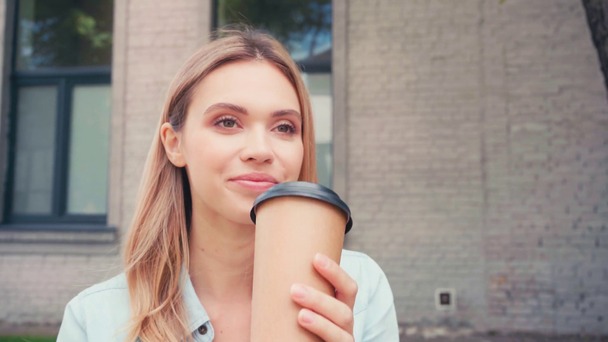 Atrakcyjny student uśmiechnięty podczas picia kawy na ulicy miejskiej  - Materiał filmowy, wideo