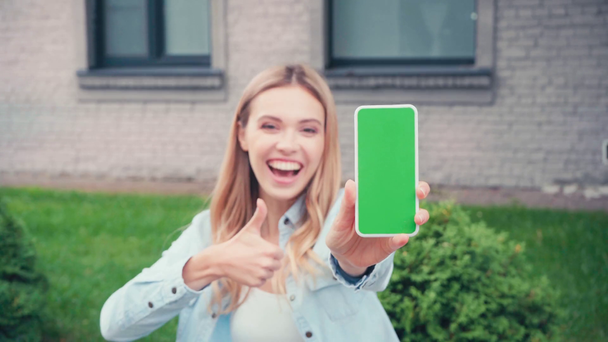 スマートフォンと親指を示す陽気な学生は、都市の通りに - 映像、動画