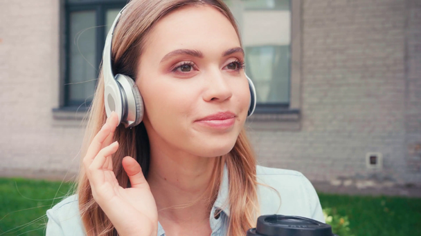 Lächelnder Student mit Kopfhörer, der Kaffee auf der Straße trinkt  - Filmmaterial, Video