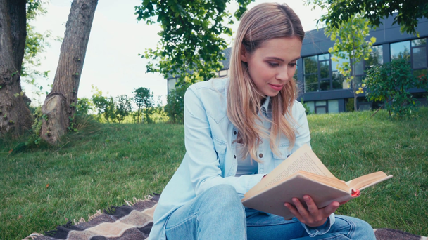 Attractive smiling student reading book on plaid in park  - Footage, Video