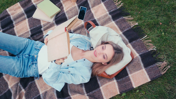 Top kilátás mosolygós diák olvasókönyv skót kockás a parkban  - Felvétel, videó