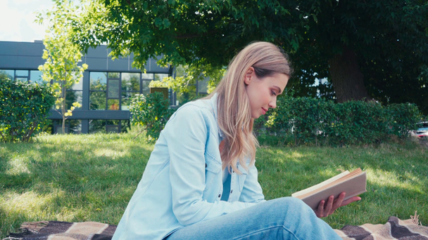 Krásný student usmívá při čtení knihy v parku  - Záběry, video