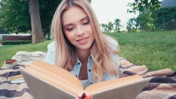 Estudiante sonriente leyendo libro sobre cuadros en el parque
  - Metraje, vídeo