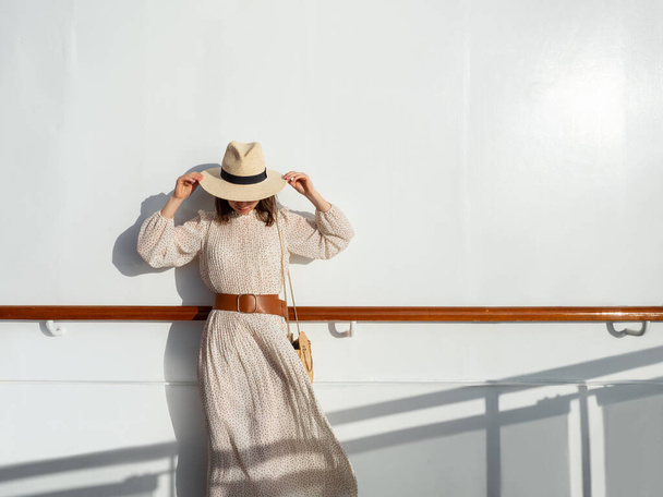 Şapkalı genç bir kadın, güneşin altında duvarın yanında. - Fotoğraf, Görsel