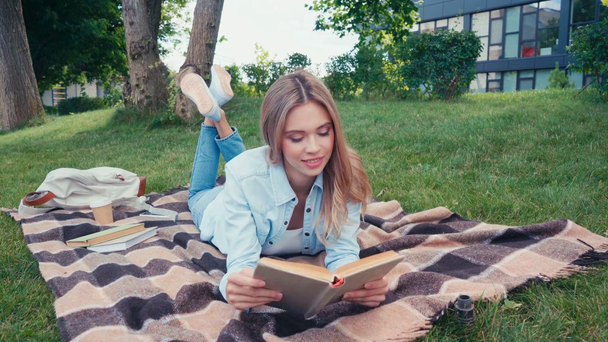 Positive student reading book while lying on plaid in park  - Footage, Video