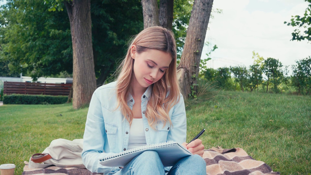 Aantrekkelijke student schrijven in notebook op plaid in park  - Video