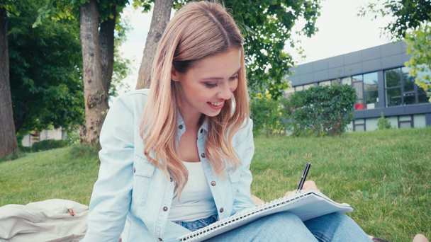 Positive student having idea while writing on notebook in park - Filmagem, Vídeo