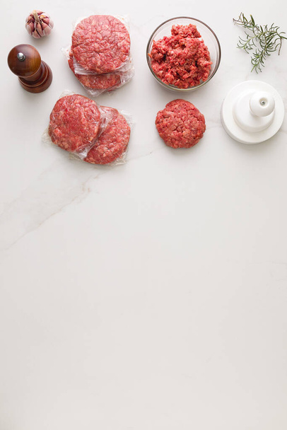 Vista dall'alto degli ingredienti per fare un hamburger. In un tavolo di marmo, una ciotola di vetro con carne, pepe di legno, aglio, modellatore di hamburger, tritacarne e rosmarino con spazio per il testo - Foto, immagini