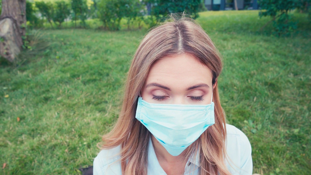 Junger Student mit medizinischer Maske blickt im Park in die Kamera  - Filmmaterial, Video