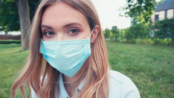 Young student in medical mask looking at camera in park  - Video