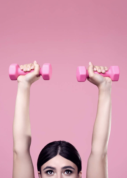 Portrait of a positive Latin woman exercising with dumbbells on a vivid background in the studio - Foto, immagini