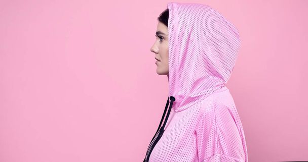 Portret van een prachtige lichaam positieve Latijnse vrouw in een roze sport hoodie poseren op een levendige achtergrond in de studio - Foto, afbeelding