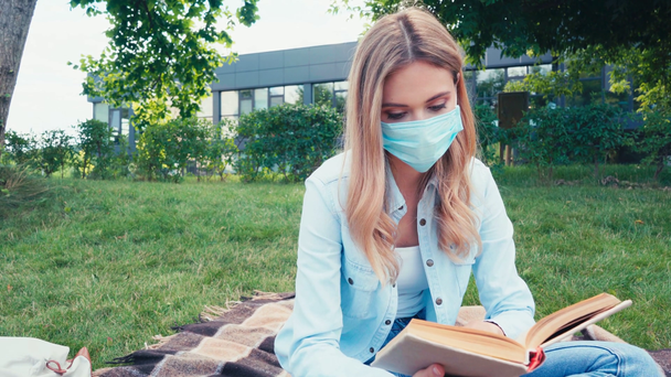 Ученик в медицинской маске читает книгу о клетчатой клетке в парке  - Кадры, видео