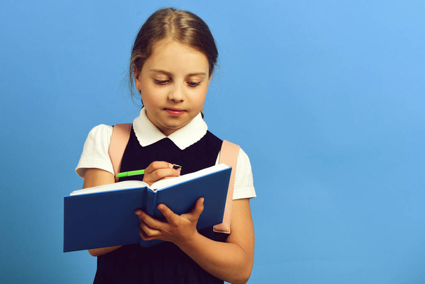 School girl with attentive face expression on blue background - Φωτογραφία, εικόνα