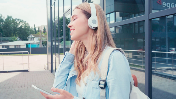 都市部のスマートフォンを使ってヘッドフォンで笑顔の学生  - 映像、動画