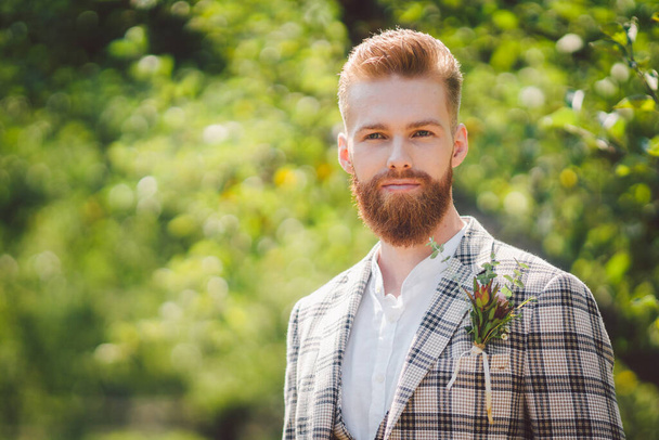 Jóképű szakállas férfi vintage ruhában. Stílusos vőlegény portré kockás kabátban az esküvője napján a parkban. Rusztikus hipszter portré. Szakállas ember. Modell stílusos frizura kockás dzsekiben - Fotó, kép