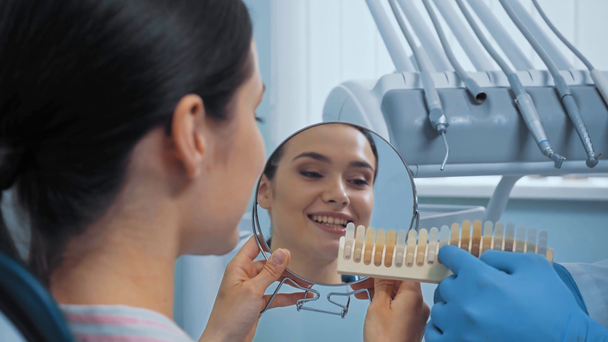 Dentista mostrando paleta de dientes a paciente con espejo en clínica
  - Metraje, vídeo
