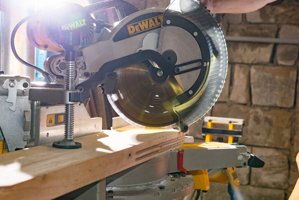 Kyiv, Ukraine - 22.07.2020: Carpenter cutting wooden board with a miter saw DeWalt, a famous American brand. - Photo, Image