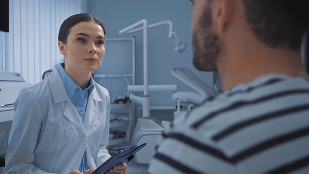 Mosolygó fogorvos írótáblával beszél a beteggel a klinikán - Felvétel, videó