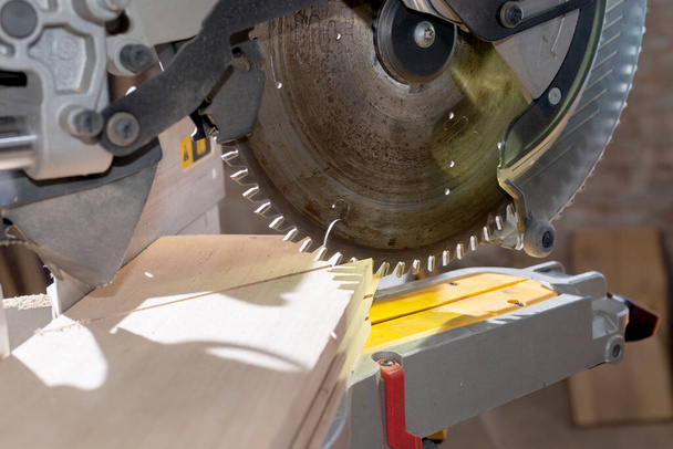 Carpenter working with power circular miter to cut wooden board against dark background. - Photo, Image