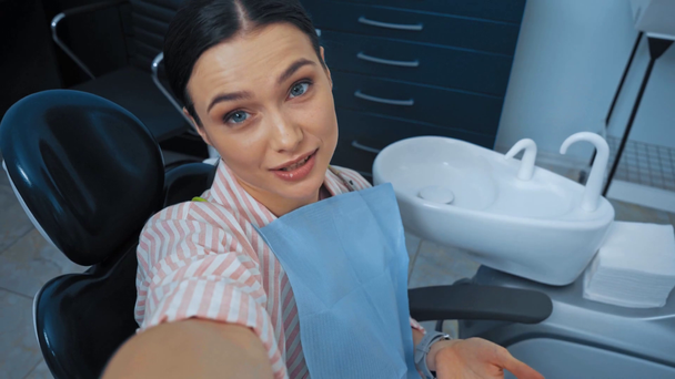 Lachende patiënt praten en zwaaien hand op camera in tandartsstoel - Video