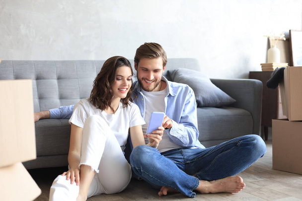 Happy couple sitting and planning new home decoration at home with a smartphone at moving day, renovation and interior design for new house. - Фото, зображення
