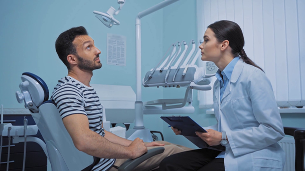 Paziente gesticolare mentre parla con il dentista con appunti in clinica  - Filmati, video