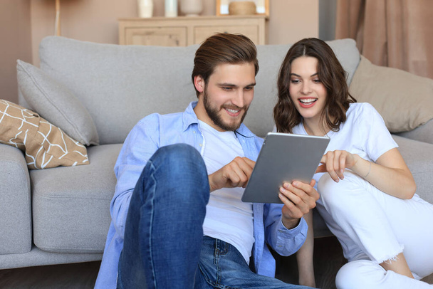 Happy couple sitting and planning new home decoration at home with a tablet, renovation and interior design for new house. - Photo, image