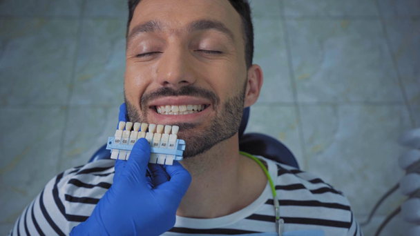Zubař ukazující paletu zubů pacientovi na klinice - Záběry, video