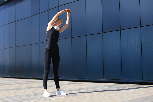 Attractive young fitness woman wearing sports clothing exercising outdoors, stretching exercises - Foto, Imagem