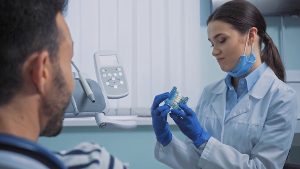 Χαμογελώντας οδοντίατρος δείχνει τα δόντια μοντέλο στον ασθενή στην κλινική  - Πλάνα, βίντεο