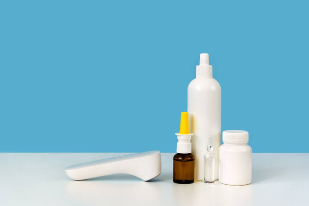 Το φάρμακο παρέχει ρύθμιση: θερμόμετρο, λευκό πλαστικό μπουκάλι, γυαλί ampule και ρινικό σπρέι. Φωτεινό μπλε φόντο. Αρχική ιατρική στήθος για γρίπη ή φαρμακευτική έννοια. Αντιγραφή χώρου για κείμενο, κοντινό πλάνο - Φωτογραφία, εικόνα