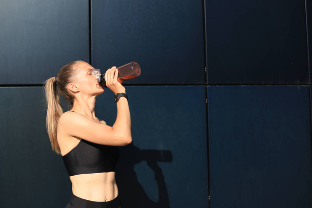 Close up of a young attractive tired sportswoman outdoors, drinking water from a bottle - Fotoğraf, Görsel