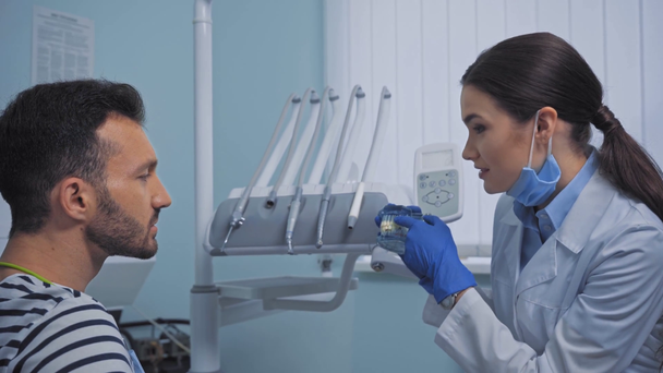 笑顔の歯科医を見ている患者はクリニックで歯モデルを示す - 映像、動画