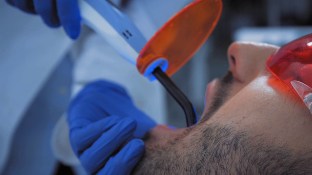 Οδοντίατρος που χρησιμοποιεί φως οδοντιατρικής θεραπείας ενώ εργάζεται με ασθενή στην κλινική  - Πλάνα, βίντεο