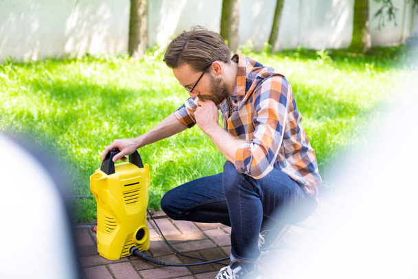Man using a high pressure washer in the backyard, on a sunny day. - Zdjęcie, obraz