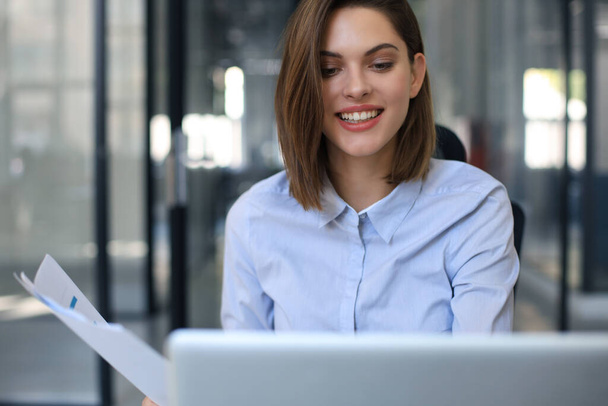 Attractive cheerful business woman checking paper documents in office, working on laptop - Foto, immagini