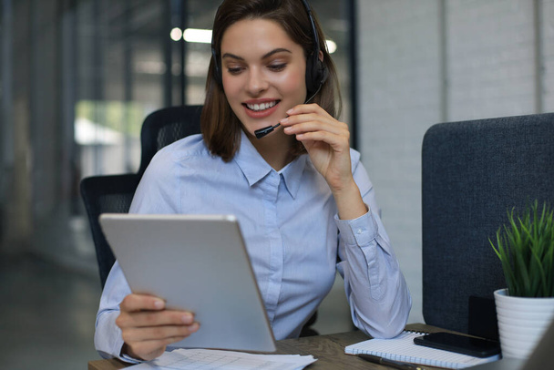 Cheerful female manager sitting at office desk and performing corporate tasks using wireless connection on digital gadgets - Фото, зображення